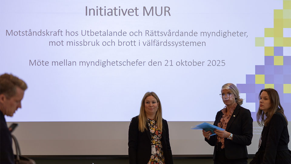 Bild på personer som står framför ett presentationsmaterial i ett sammanträdesrum.