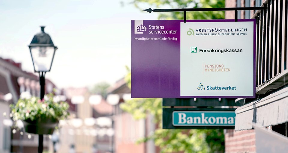 A sign hanging off a wall with an old town centre in the background.